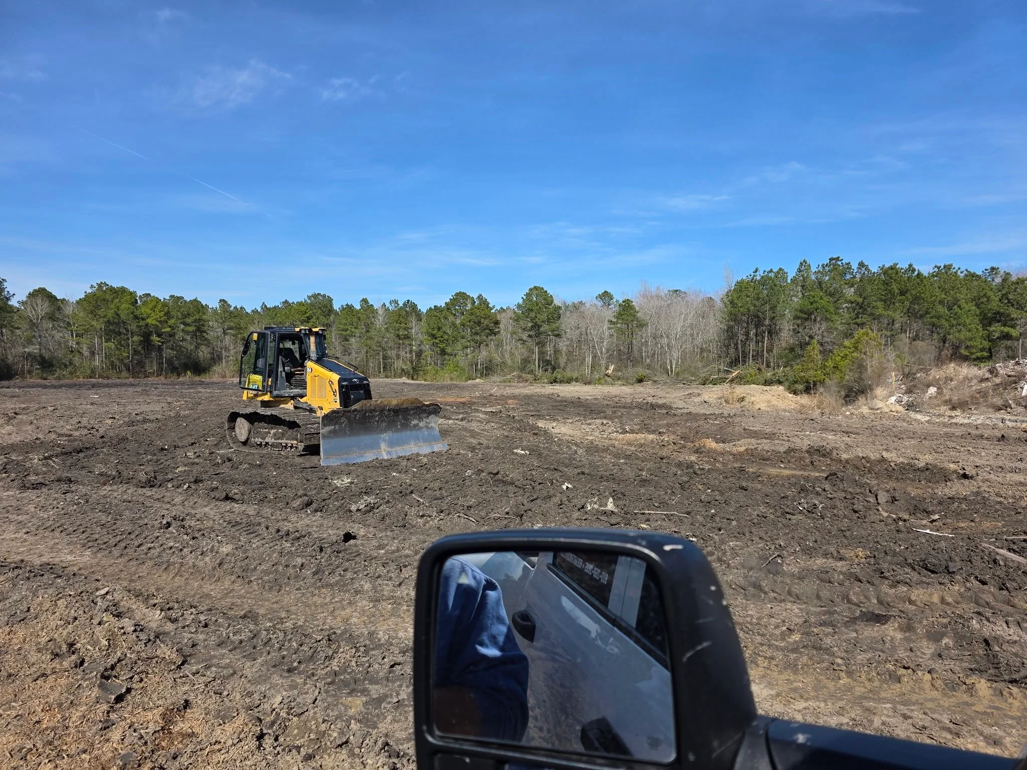 Yellow and black tracked bulldozer with front blade grading dirt on cleared construction site
