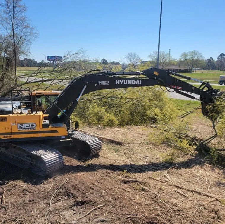 Hyundai excavator with grapple attachment clearing brush and vegetation from cleared land
